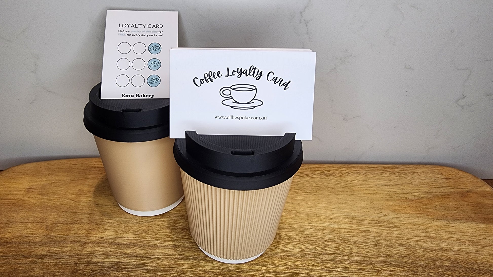 Two coffee cups with black lids and a loyalty card on a wooden surface.